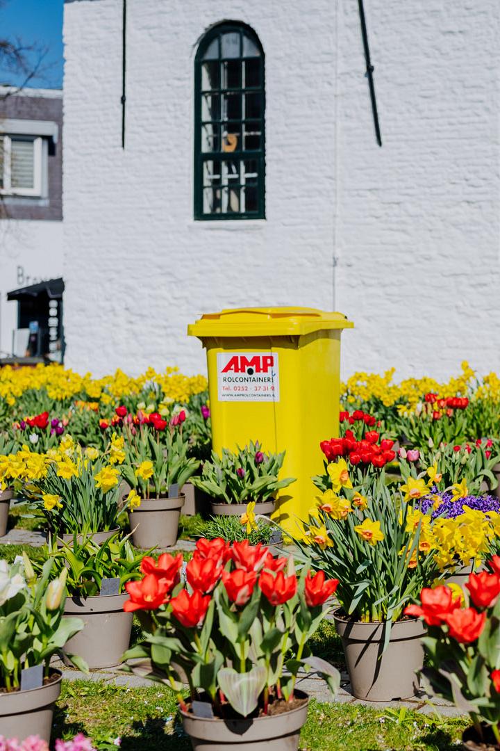 Twee AMP-medewerkers bij een vuilniswagen terwijl een grote groene container wordt geleegd.
