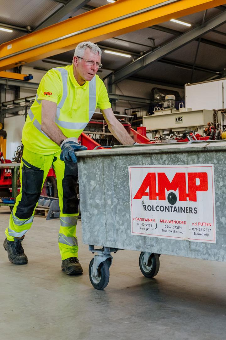 AMP-medewerker duwt een grote metalen rolcontainer door een industriële werkplaats.
