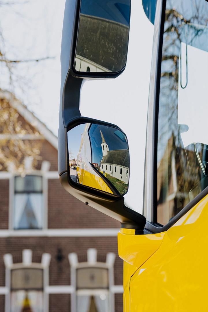 Witte kerk weerspiegelt in de buitenspiegels van een gele AMP-vrachtwagen.