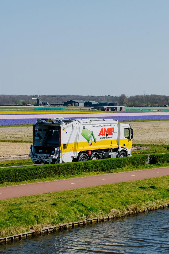 AMP-vuilniswagen rijdt langs kleurrijke bollenvelden in een landelijk landschap.