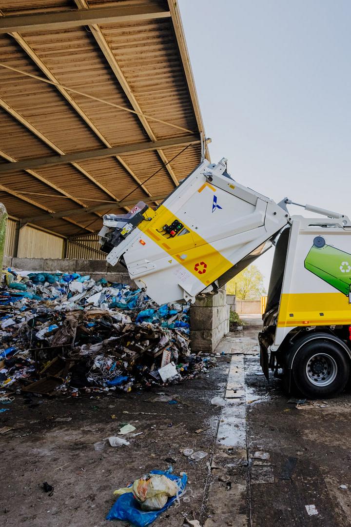 AMP-vuilniswagen stort afval in een overdekte loods op een verwerkingslocatie.