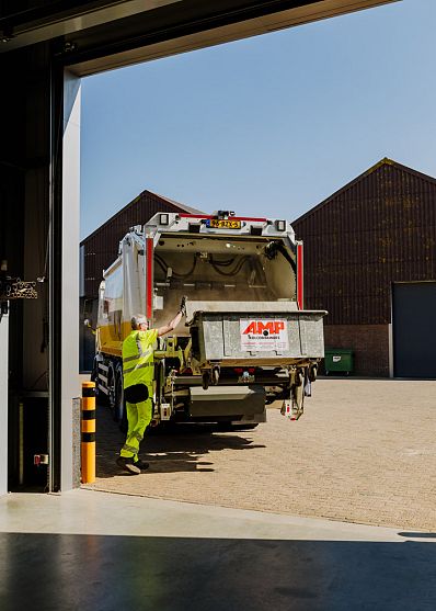 AMP-medewerker controleert de binnenkant van de vuilniswagen tijdens het legen van afval, met focus op veiligheid, onderhoud en een schone werking van het inzamelsysteem.