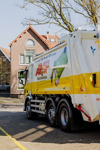 Zijaanzicht van een AMP-vuilniswagen met opvallende slogan en illustratie, geparkeerd in een woonwijk.