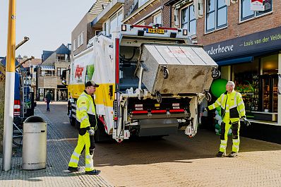 Afvalinzameling in een winkelstraat door twee medewerkers met een vuilniswagen