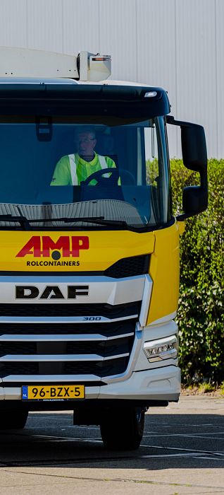 Vooraanzicht van een AMP-vrachtwagen met bestuurder in veiligheidshesje achter het stuur.