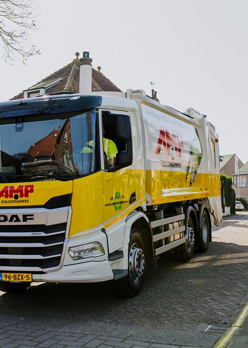 Een medewerker in fluorescerende werkkleding loopt langs een gele en witte afvalwagen in een woonstraat.