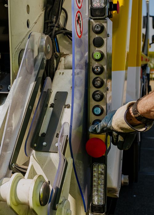 Arm strekt uit naar knop van vuilniswagen op klep op te tillen.
