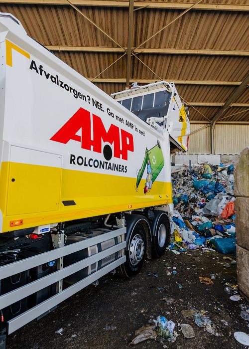 AMP-vuilniswagen lost afval in een loods bij een afvalverwerkingsbedrijf met stapels plastic.