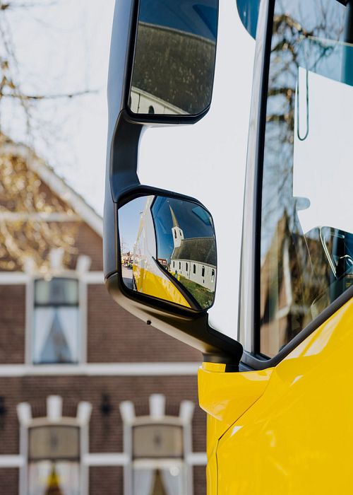 Ingezoomde foto van een vrachtwagen deur met kijkspiegels en oude boerderij woning op de achtergrond.