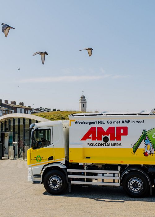 AMP-vuilniswagen geparkeerd bij een hoop restafval half onder een afdak.