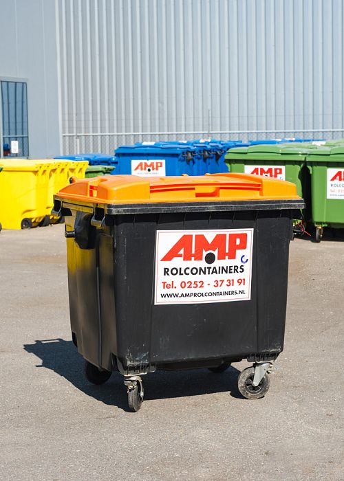 Zwarte rolcontainer met oranje deksel op het buitenterrein van AMP, omringd door containers in diverse kleuren voor verschillende afvalstromen.