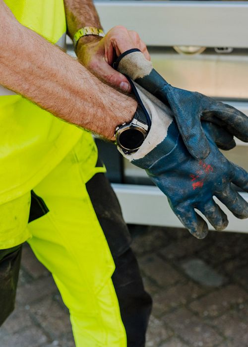 AMP-medewerker trekt stevige werkhandschoenen aan voor een veilige inzamelronde, met focus op beschermende werkkleding en voorbereiding.