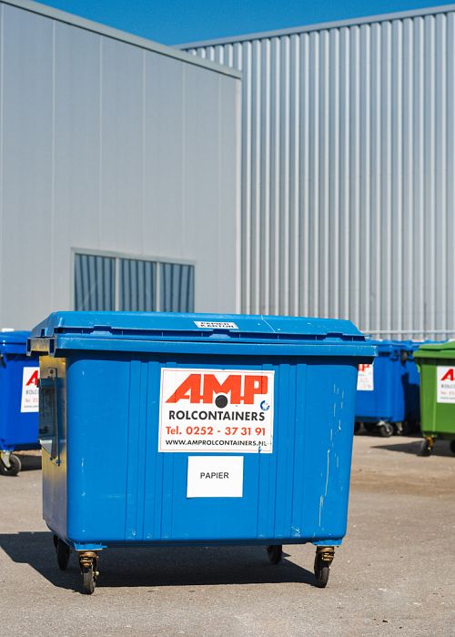 Blauwe AMP-container op terrein met meerdere gekleurde rolcontainers bij industriepand.