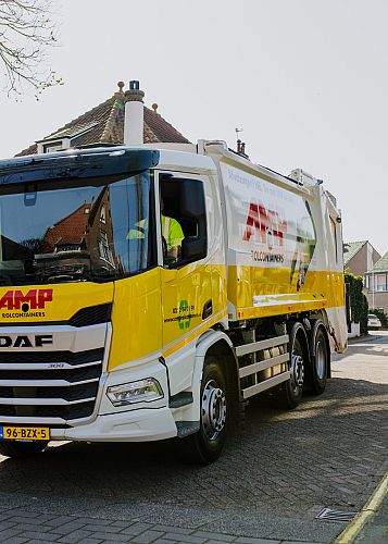 Lachende AMP-medewerker rolt een gele container langs een fietsenwinkel over de stoep.