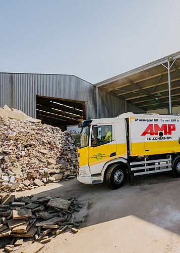 AMP-vuilniswagen geparkeerd bij een hoop restafval half onder een afdak.